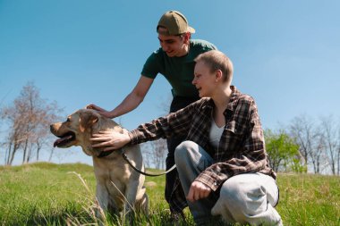 Güneşli bir tarlada iki insanın dost canlısı bir köpekle eğlendiği mutlu bir an..