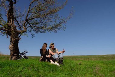 Genç bir çift parkta bir ağacın altında birlikte oturur. Bisikletleriyle güneşli bir günün tadını çıkarıyorlar..