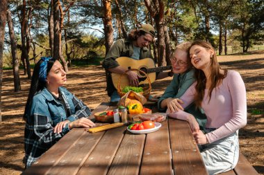 Ormandaki piknik masasında dinlenen bir grup arkadaş dışarıda keyifli bir toplantı için yemek ve müziğin tadını çıkarıyorlar..