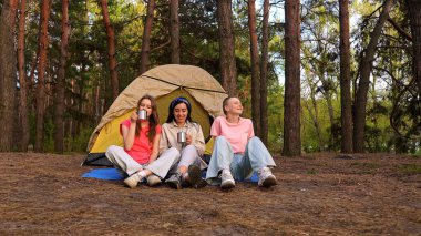 Üç arkadaş ormanda bir çadırda oturup, bir kamp gezisi sırasında içkinin ve arkadaşlığın tadını çıkarıyorlar..