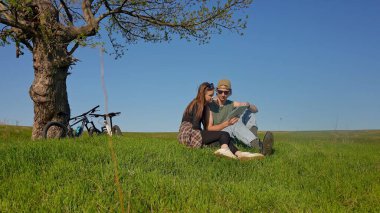Bir çift bir ağacın altında oturur, uçsuz bucaksız yeşil bir alanda bisiklet maceraları sırasında haritayı keşfederler..