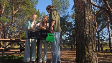 Bir grup arkadaş güneşli bir günün tadını çıkarıyorlar. Uzun ağaçlarla çevrili, pitoresk bir parkta barbekü yapıyorlar..