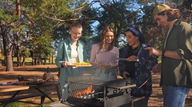 Bir grup arkadaş güneşli bir günün tadını çıkarıyorlar. Uzun ağaçlarla çevrili, pitoresk bir parkta barbekü yapıyorlar..
