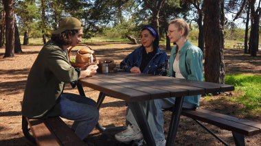 Güneşli bir park ortamında piknik masasında dinlenen üç arkadaş. Birbirine eşlik eden ve dışarıda eğlenen üç arkadaş..