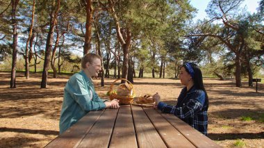 Güneşli bir park ortamında piknik masasında dinlenen iki arkadaş, birbirine eşlik eden ve dışarıda eğlenen iki arkadaş..