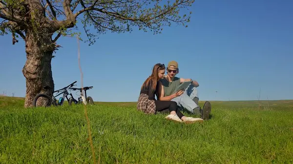 Bir çift bir ağacın altında oturur, uçsuz bucaksız yeşil bir alanda bisiklet maceraları sırasında haritayı keşfederler..