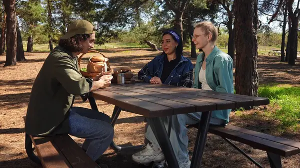 Güneşli bir park ortamında piknik masasında dinlenen üç arkadaş. Birbirine eşlik eden ve dışarıda eğlenen üç arkadaş..