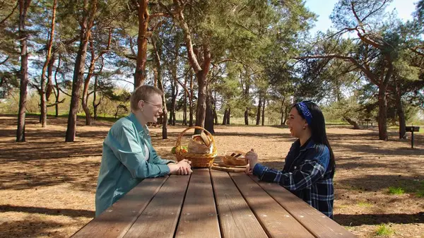 Güneşli bir park ortamında piknik masasında dinlenen iki arkadaş, birbirine eşlik eden ve dışarıda eğlenen iki arkadaş..