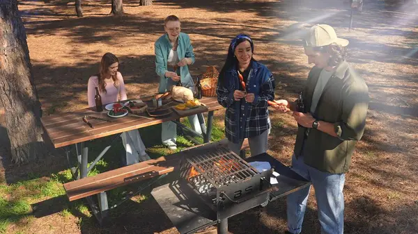 Bir grup arkadaş güneşli bir günün tadını çıkarıyorlar. Uzun ağaçlarla çevrili, pitoresk bir parkta barbekü yapıyorlar..