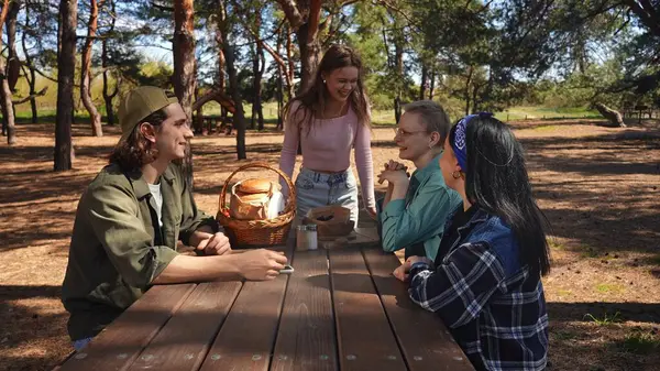 Bir grup arkadaş güneşli bir park ortamında piknik masasında dinleniyorlar, birbirlerine eşlik ediyorlar ve dışarıda eğleniyorlar..