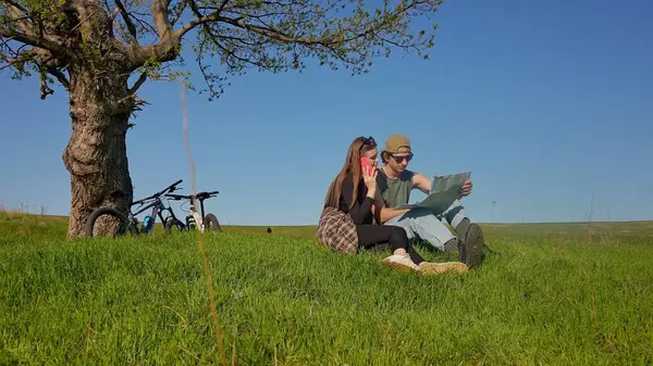 Bir çift bir ağacın altında oturur, uçsuz bucaksız yeşil bir alanda bisiklet maceraları sırasında haritayı keşfederler..