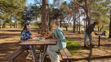 Ormanlık bir parkta piknik yapan bir grup arkadaş, doğada yemek ve sohbetin tadını çıkarıyorlar..