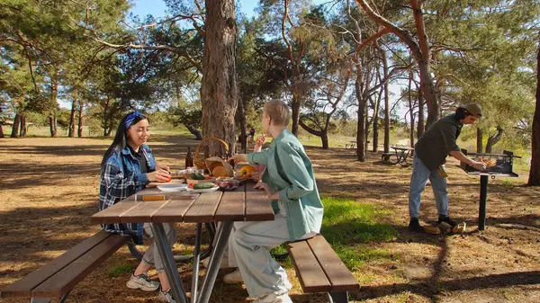 Ormanlık bir parkta piknik yapan bir grup arkadaş, doğada yemek ve sohbetin tadını çıkarıyorlar..