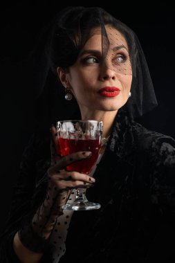 Göz kamaştırıcı makyajlı sofistike bir kadın elinde kırmızı bir bardak tutuyor, zarafet ve gizem taşıyor..
