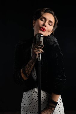 Klasik bir mikrofona tutkuyla şarkı söyleyen, klasik giyinmiş bir kadın retro müzik tarzının özünü yakalıyor..