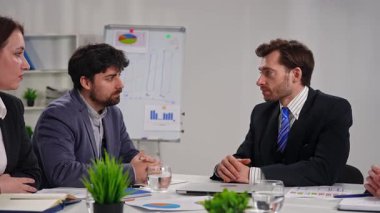 Ofisteki bir iş toplantısında, çizelgelerle strateji tartışması yapan dört profesyonel. Yavaş çekim