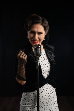 Tarz sahibi bir retro şarkıcısı tutkulu bir şekilde klasik bir mikrofonla şarkı söylüyor. Klasik kıyafet ve zarafet performansı vurguluyor.