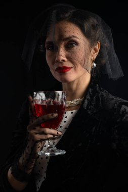 Zarif giyinmiş dengeli bir kadın elinde bir kadeh kırmızı şarap tutarken entelektüellik sergiliyor..