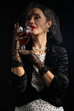 Sofistike bir kadın klasik klasik bir giysi içinde şarap yudumlarken inciler ve dantel eldivenler takıyor..