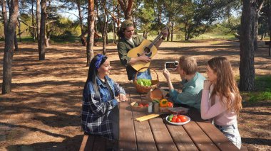 Bir grup arkadaş piknik için toplanır, güneşli bir açık hava ortamında yemek ve müziğin tadını çıkarırlar, rahatlamayı teşvik ederler..