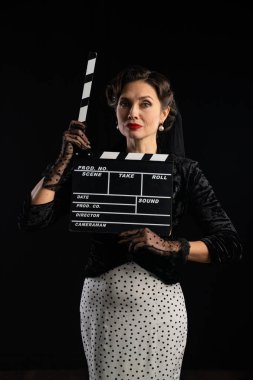 Zarif giyimli eski moda bir aktris film sehpası tutuyor. Film yapımcılığının hazır olduğunu simgeliyor..