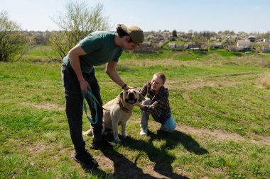 Doğa ve manzaralı bir köy manzarası ile çevrili çimenli bir tarlada köpeğiyle güneşli bir günün tadını çıkaran iki insan..