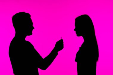 Romantik bir siluet, canlı pembe bir arka plana dayanan bir yüzükle evlenme teklifinin anını yakalar..