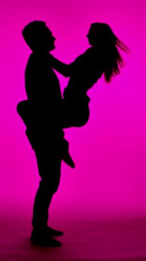 Tutkuyla kucaklaşan bir çiftin çarpıcı silueti, pembe bir arkaplanda yakalanmış..