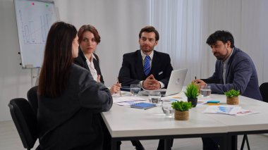 Ofiste bir iş toplantısına katılan dört profesyonel, çizelgelerle stratejiyi tartışıyor..