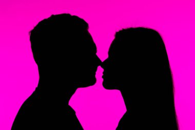 Çarpıcı bir siluet, canlı pembe bir arkaplan karşısında birbirine bakan bir çift, bir romantizm ve yakınlık hissi yakalıyor..