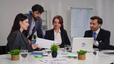 Ofiste bir iş toplantısına katılan dört profesyonel, çizelgelerle stratejiyi tartışıyor..