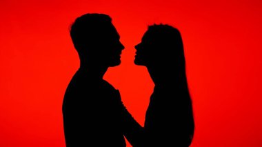 Çarpıcı bir siluet, canlı kırmızı bir arkaplan karşısında romantik bir yakınlık anı yakalıyor..