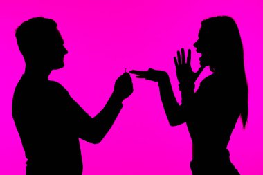 Canlı pembe bir arkaplan üzerine kurulmuş, şaşırtıcı ve duygusal bir anı yakalayan, yüzükle evlenme teklif eden bir kişinin silüeti..