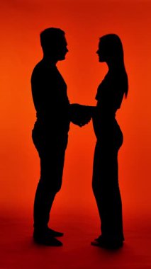 Bir çiftin birbirine doğru yürümesi ve parlak kırmızı bir arka planda yanaktan öpmesi romantik ve romantik bir sahne yaratır..