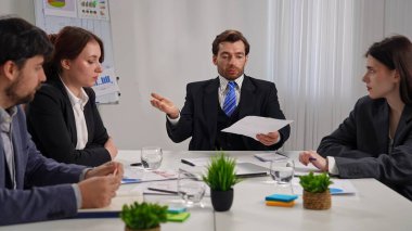 Ofiste bir iş toplantısına katılan dört profesyonel, çizelgelerle stratejiyi tartışıyor..