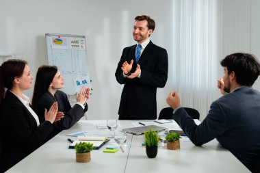 Bir iş toplantısı sırasında bir takımın alkış tutması, başarı ve işbirliğini sembolize ediyor..