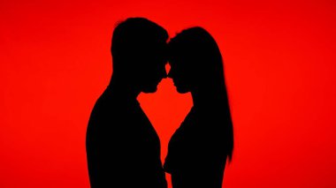 Bir çift silueti, canlı kırmızı bir arkaplan karşısında romantik bir ortam yaratıyor..