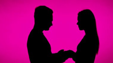 Birbirlerine doğru yürüyen ve pembe bir arka planda el ele tutuşan bir çiftin silueti romantik ve romantik bir sahne yaratır.