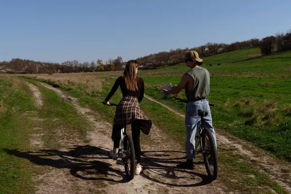 Genç bir çift bisikletleriyle kırsal bir yolu keşfeder, doğanın güzelliğini tecrübe eder ve güneşli günün tadını çıkarır..