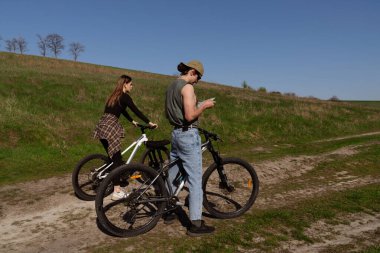 İki bisikletçi, açık mavi gökyüzünün altındaki haritayı kontrol etmek için manzaralı bir kırsal yolda durup güneşli bir maceranın tadını çıkarıyor..