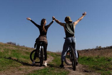 Bir erkek ve bir kadın kırsal bir yolda bisiklet sürmekten zevk alırlar, güneşli havada özgürlüğü ve doğayı kucaklarlar..