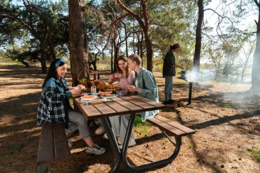 Ormanlık bir parkta piknik yapan bir grup arkadaş, doğada yemek ve sohbetin tadını çıkarıyorlar..