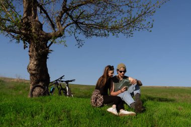 Bir çift bir ağacın altında oturur, uçsuz bucaksız yeşil bir alanda bisiklet maceraları sırasında haritayı keşfederler..