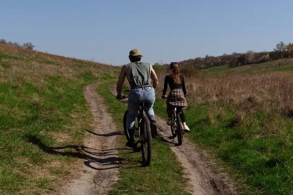 Bir çift, doğa tarafından çevrelenmiş, doğa manzaralı bir patikada bisiklet sürüyor, kırsal kesimde macera ve rahatlığın özünü yakalıyor..