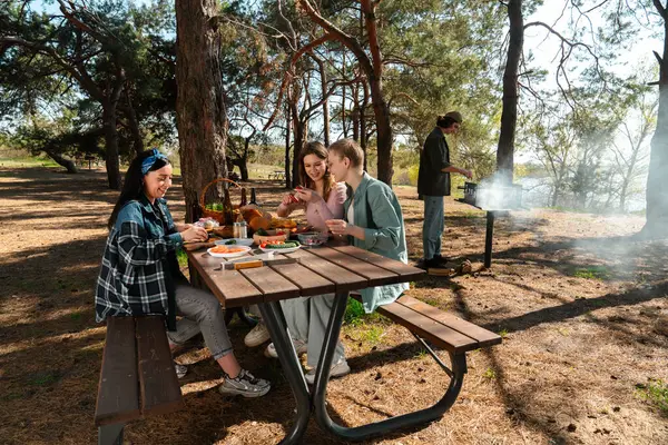 Ormanlık bir parkta piknik yapan bir grup arkadaş, doğada yemek ve sohbetin tadını çıkarıyorlar..