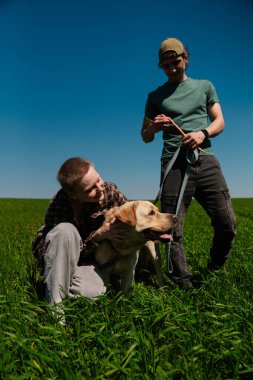 İki arkadaş çimenli bir arazide köpeğiyle güneşli bir günün tadını çıkarıyorlar. Sahne neşe ve arkadaşlığı yakalar..