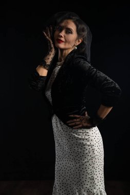 Bir kadın şık siyah bir duvak ve eldivenle şık bir benekli elbiseyle şık bir şekilde poz verir..