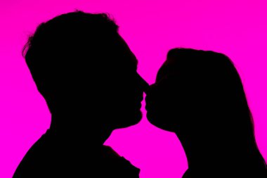 Romantik bir öpüşme silueti, dikkat çekici pembe bir arka plan ile onların profillerini vurguluyor ve görüntüye yoğunluk katıyor..