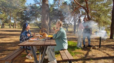 Ormanlık bir parkta piknik yapan bir grup arkadaş, doğada yemek ve sohbetin tadını çıkarıyorlar..