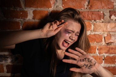 Yüzü morarmış bir kadın korunmak istiyor. Beni elinde tuğla bir duvara karşı koruyor..